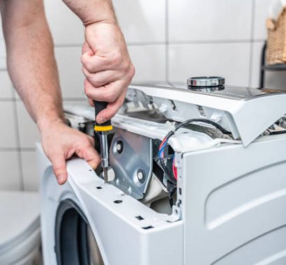 Repairman using a screwdriver disassembles a washing machine for repair